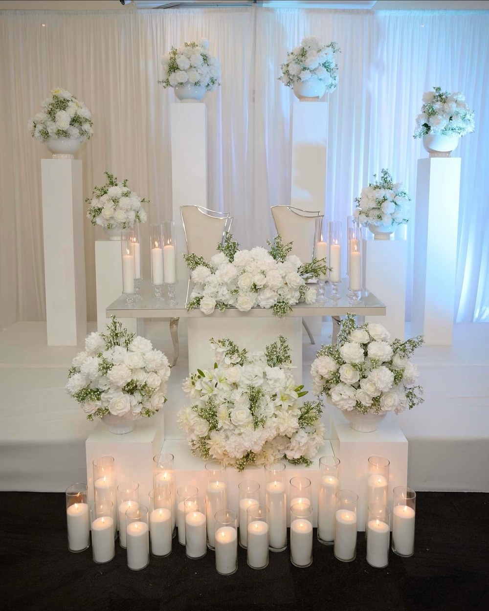Tiered display of white florals above a row of pillar candles