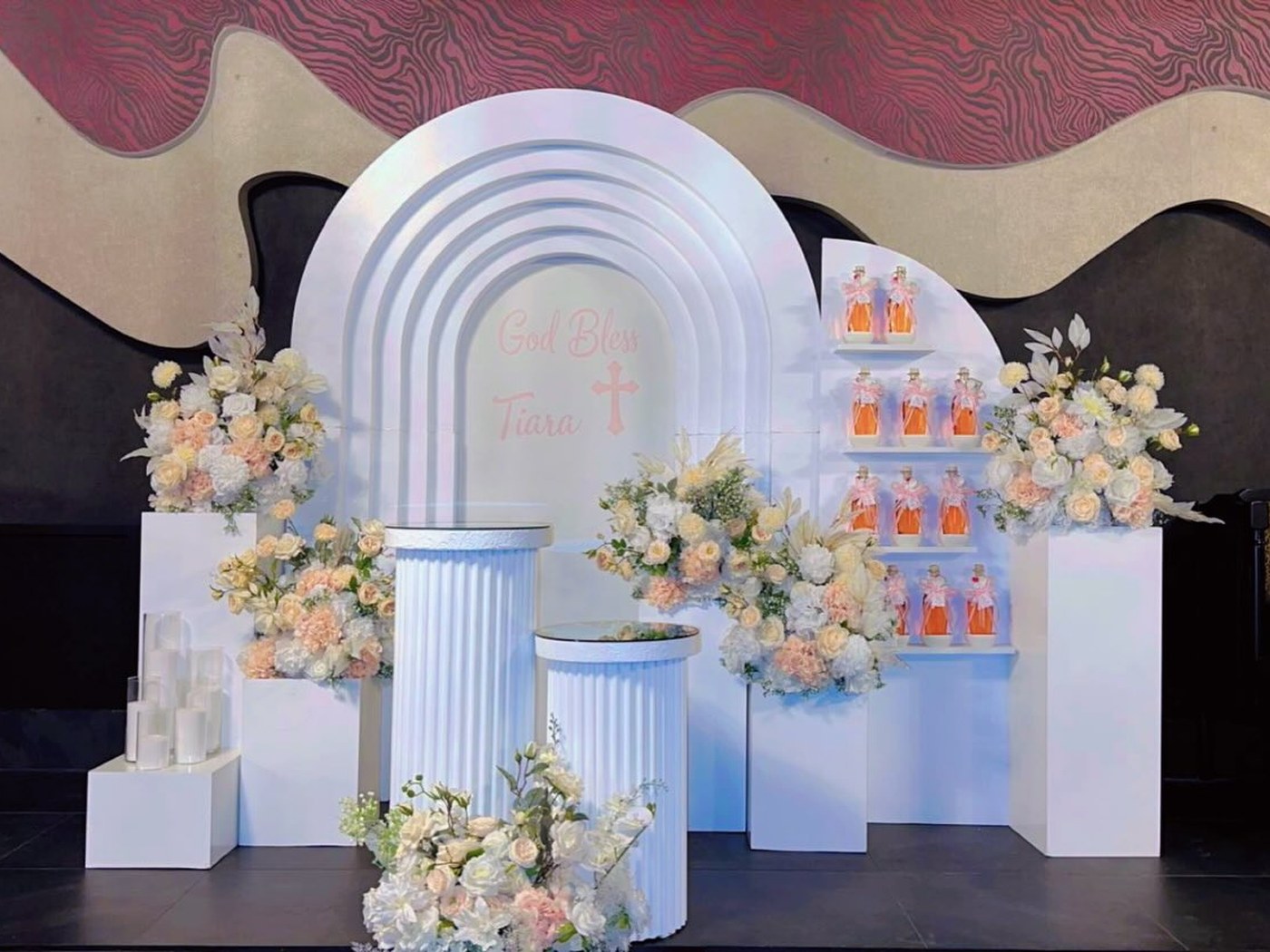 Baptism backdrop of white arches with peach florals and a favour display