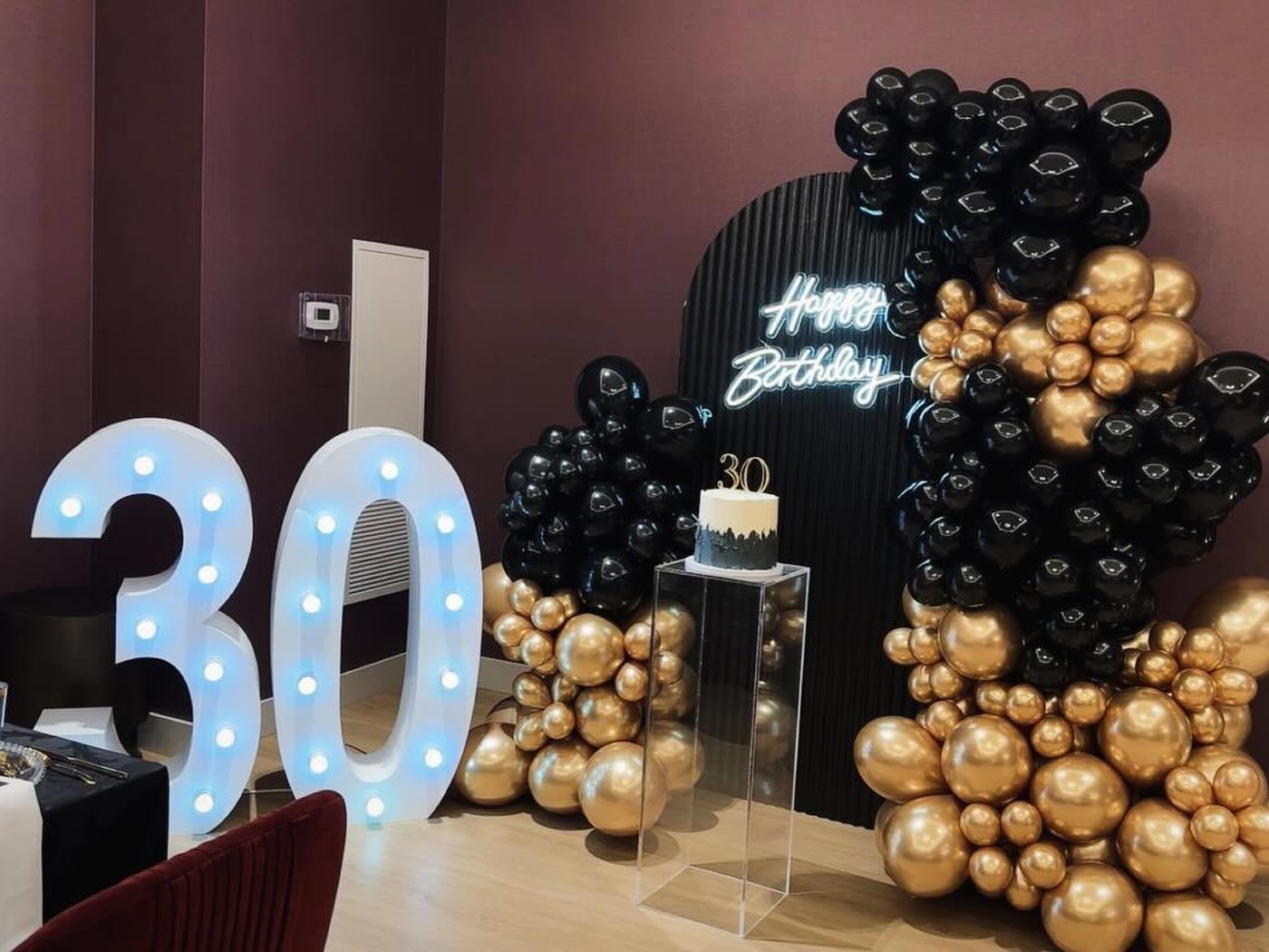 Thirtieth birthday setup with light-up numbers and black and gold balloons