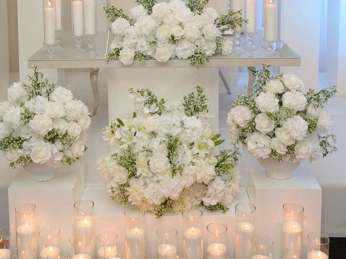 Tiered white floral display above a bank of pillar candles