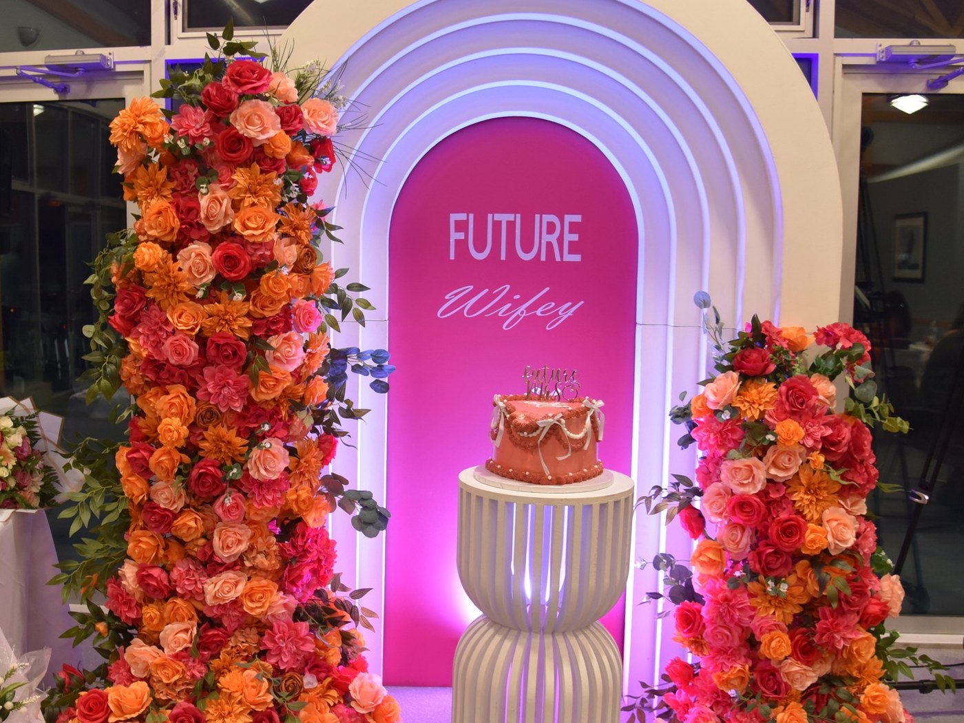 Engagement backdrop with columns of coral and crimson roses around a cake plinth