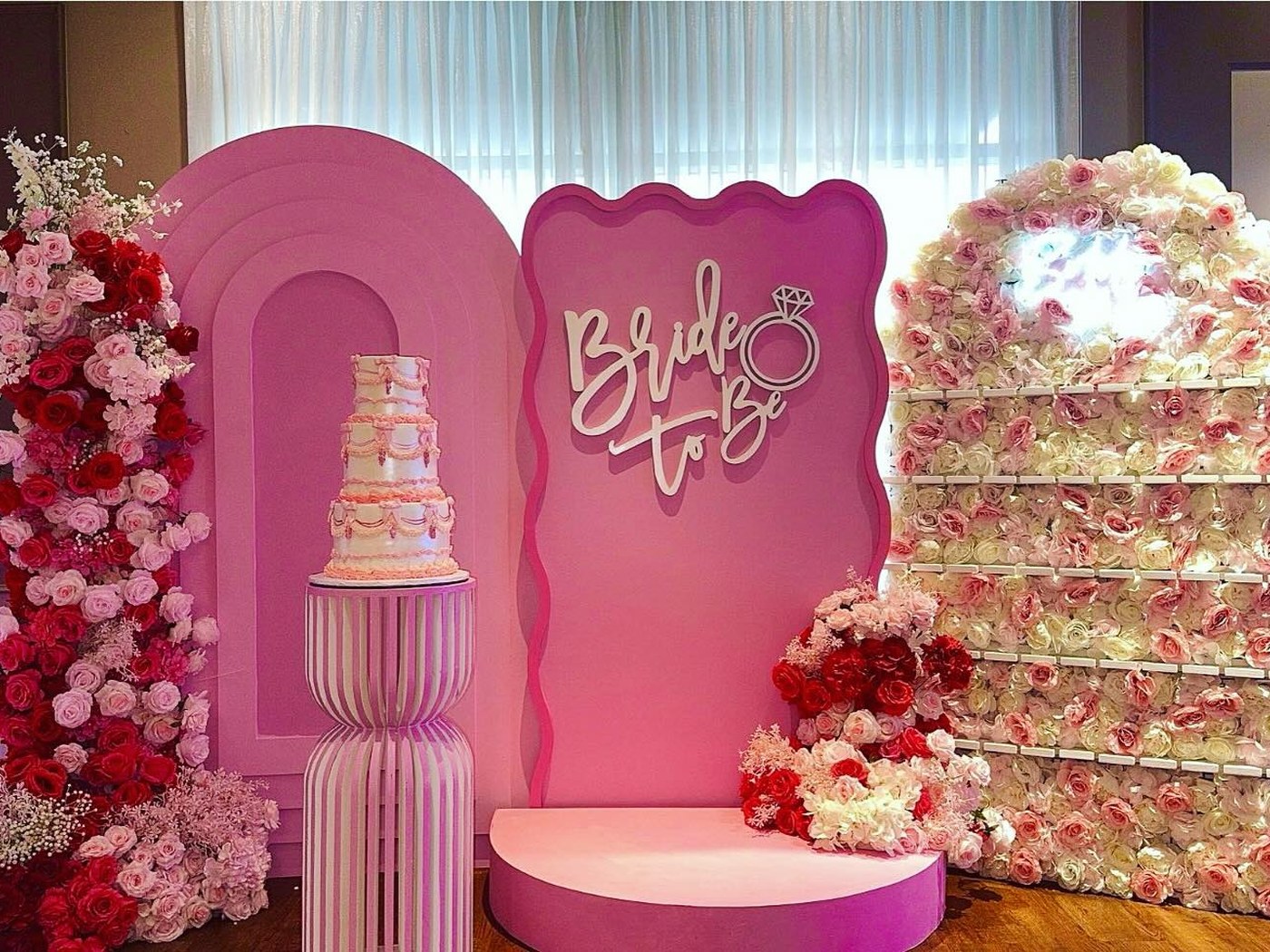 Bridal shower backdrop in pink with a tiered cake and a rose-covered dessert wall