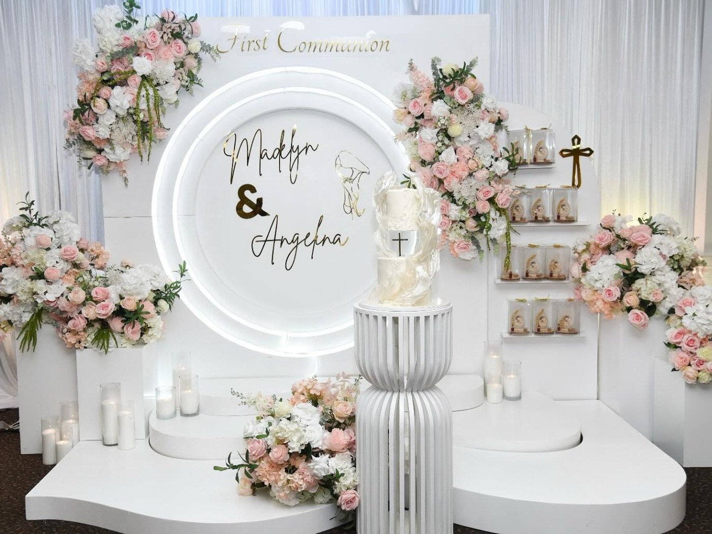 First communion setup with an illuminated circular sign, blush florals and favour shelves
