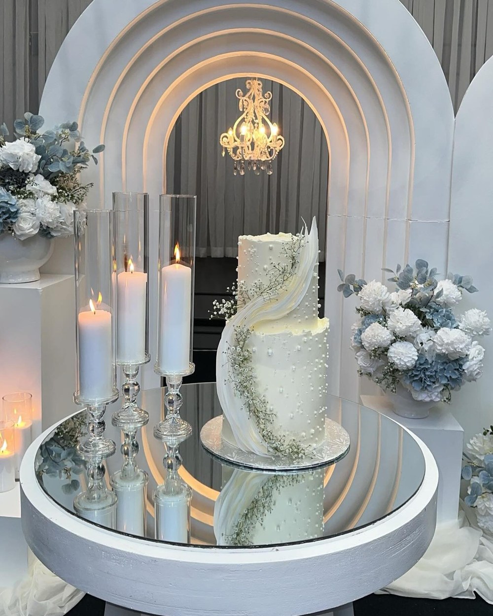 Tiered wedding cake on a mirrored plinth with blue florals and tall candles