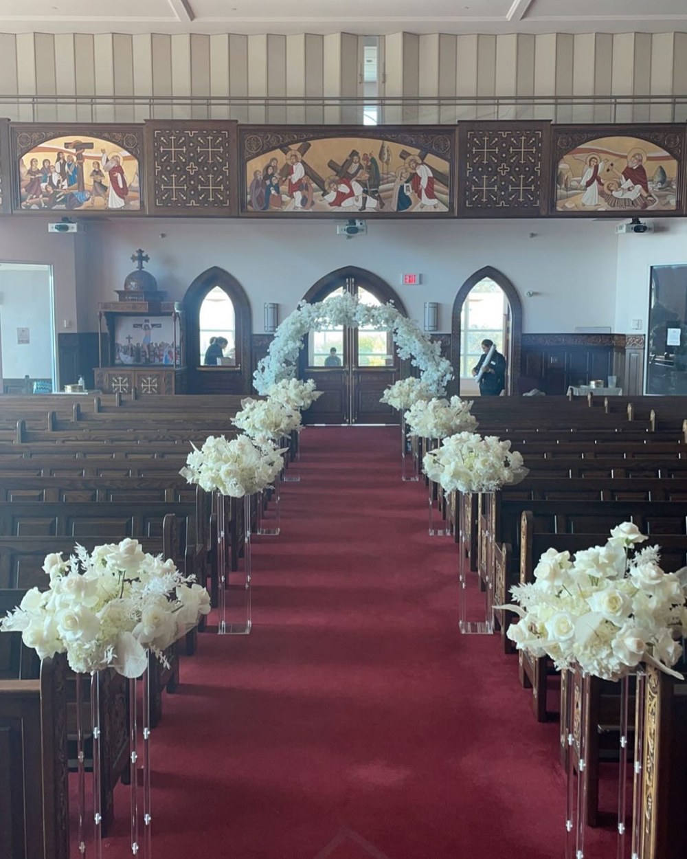 Church aisle lined with tall white floral arrangements on clear stands