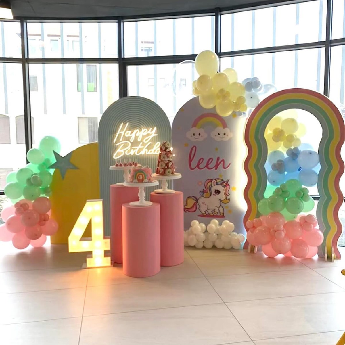 Pastel rainbow birthday setup with balloon garlands and a dessert display