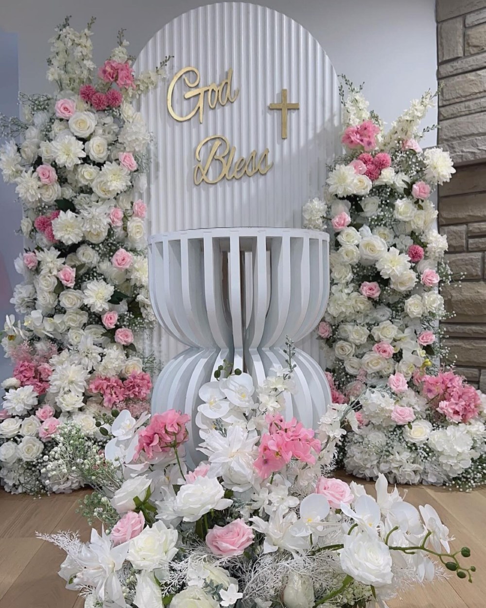 Baptism backdrop with a gold cross, blush and ivory florals and a fluted plinth