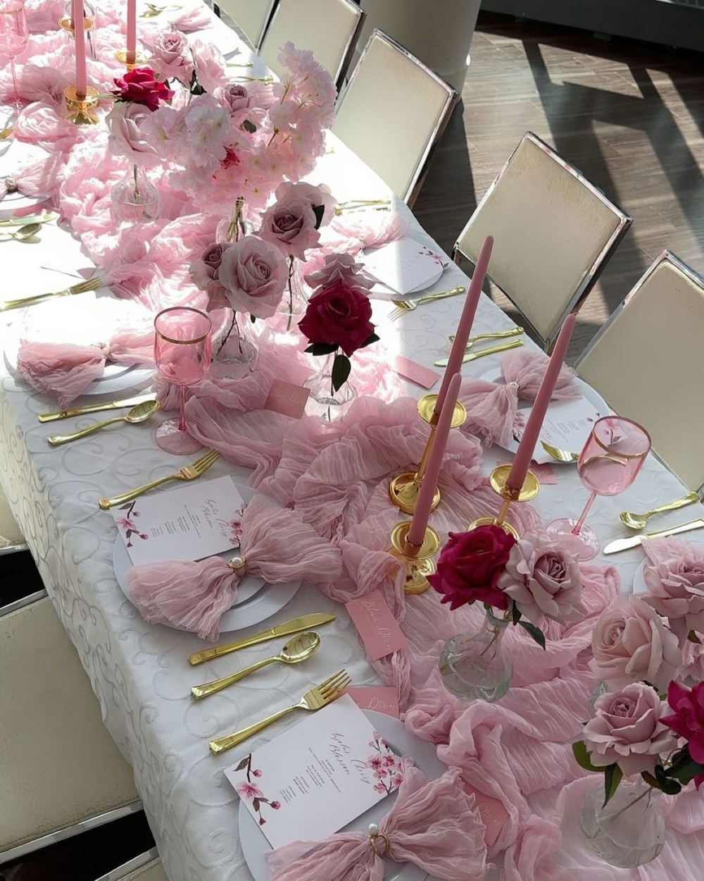 Long guest table dressed with blush tulle, roses, gold cutlery and taper candles