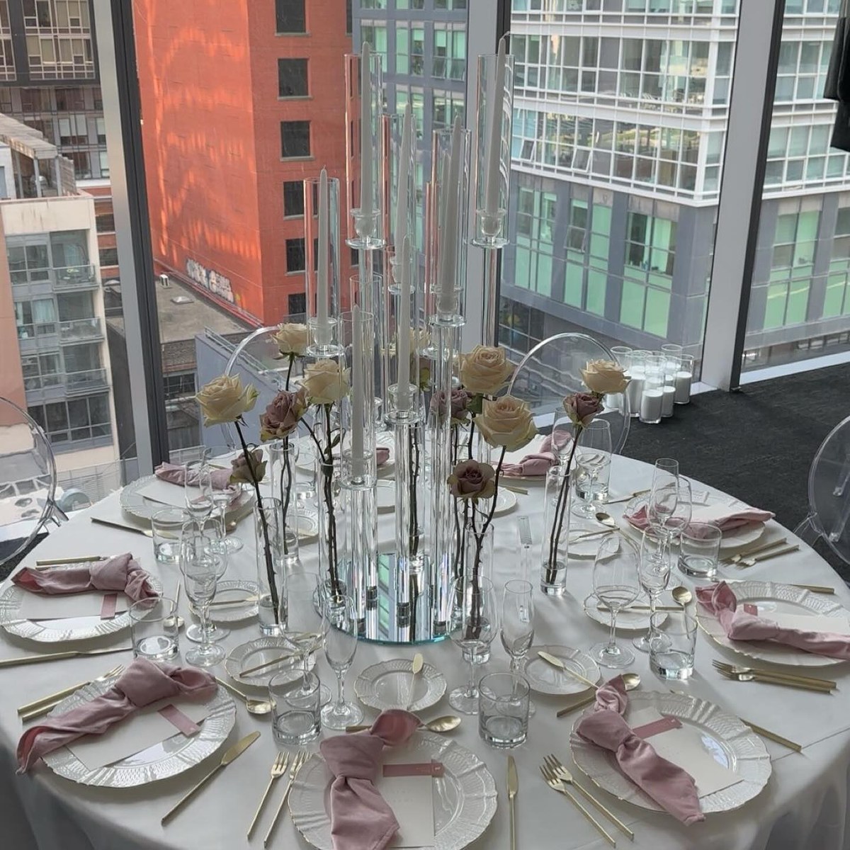 Round reception table with tall glass candelabra beside floor-to-ceiling city windows