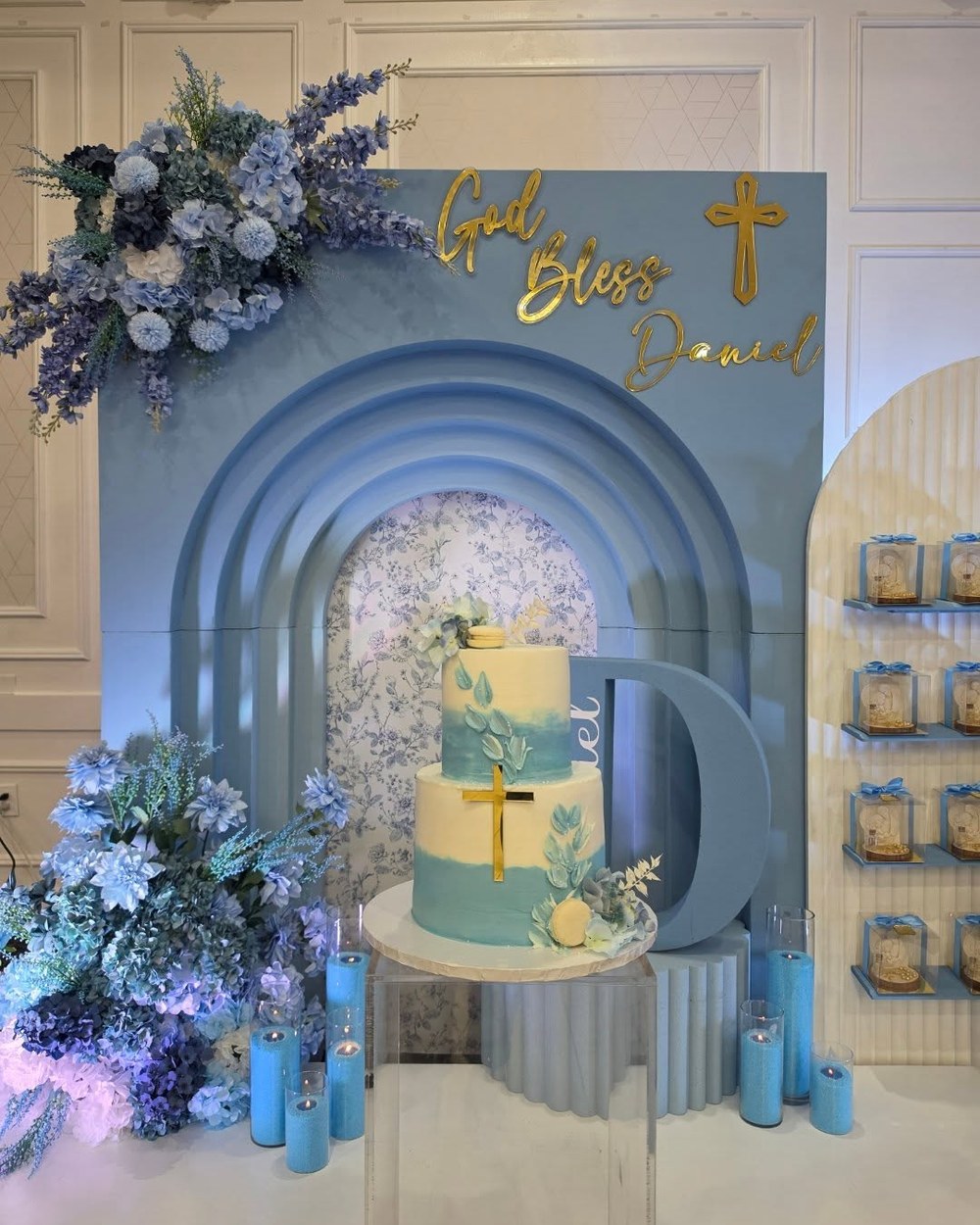 Baptism backdrop in soft blue with a gold cross, cake and lavender florals
