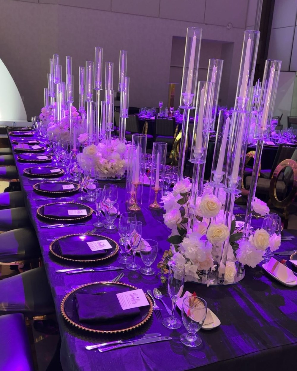 Long reception table under violet uplighting with tall candelabra and pale florals